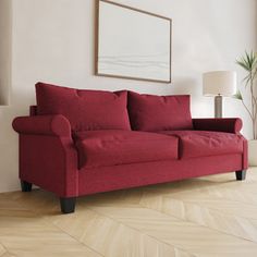 a red couch sitting on top of a hard wood floor next to a lamp and window