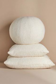 three white pillows stacked on top of each other in front of a beige wall,