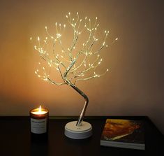 a lighted tree on a table next to a lit candle and book with the light turned on