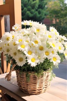 a basket filled with white and yellow daisies on top of a wooden picnic table