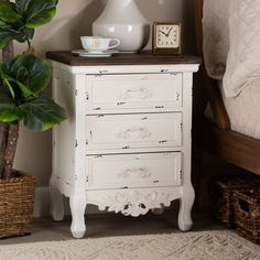 a white dresser sitting next to a bed with a plant on top of it and a clock