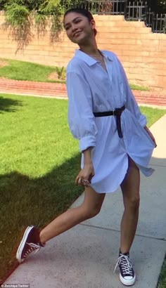 a woman is posing on the sidewalk in her white shirt dress and converses sneakers