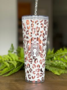 a starbucks cup with leopard print on it and a chain hanging from the bottom, sitting on a table