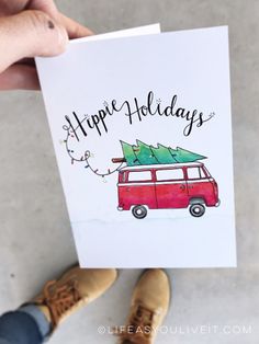 someone holding up a card with a red van and christmas tree on top that says happy holidays