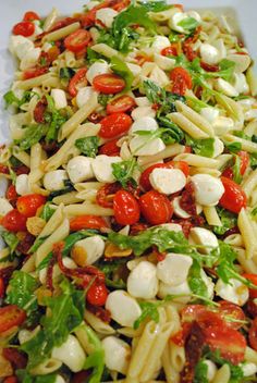 a pasta salad with tomatoes, mozzarella and spinach on a white plate