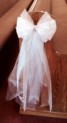 a white bow tied to the back of a wooden church pew with fabric on it