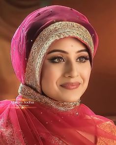 a woman wearing a red and gold outfit with a veil on her head, smiling at the camera