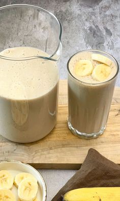 two glasses of banana smoothie next to bananas on a cutting board