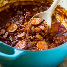 a wooden spoon stirring beans and sausages in a pot with brown gravy