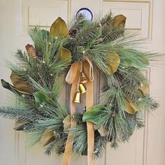 a wreath is hanging on the front door with bells and evergreen leaves, as well as pine cones