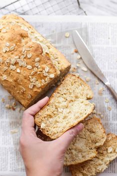 a person holding a loaf of bread on top of a newspaper next to a knife