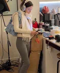 a woman wearing headphones standing in front of a desk with a bag on it