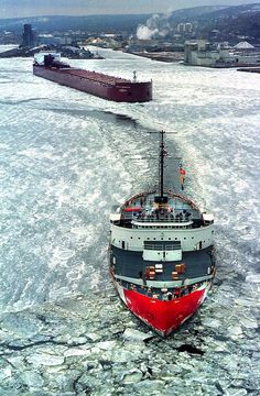 a large boat floating on top of an ice covered ocean next to a ship in the distance