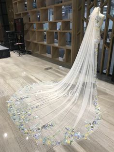 a wedding veil with flowers on it in front of a bookshelf filled with shelves