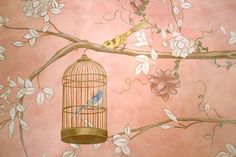 a bird in a cage sitting on a tree branch next to a flowery wall