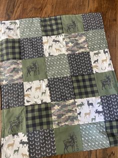 a green and white patchwork quilt with deer on the front is laying on a wooden floor