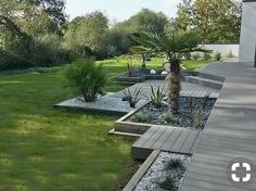 an outdoor area with wooden decking and plants on the grass, surrounded by trees