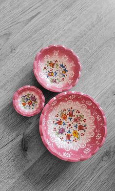 three pink dishes sitting on top of a wooden table