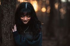 a woman standing next to a tree in the woods