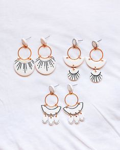 five pairs of earrings on top of a white sheet with gold trimmings and fringe detailing