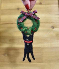 a hand holding a small black cat ornament with a green wreath on it