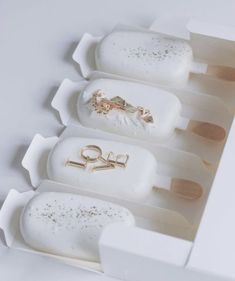 four pops are in a white box with gold rings and scissors on them, all lined up next to each other