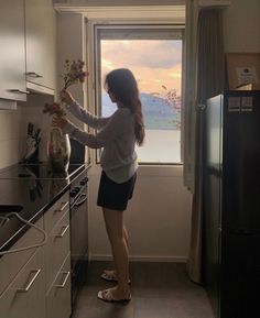 a woman standing in front of a window holding a vase with flowers on the counter