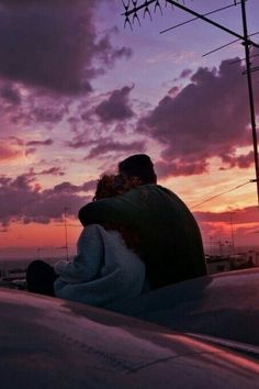 two people sitting on the roof of a car at sunset