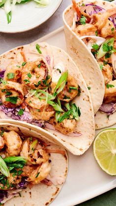 three tacos with shrimp, onions and cilantro on a white platter