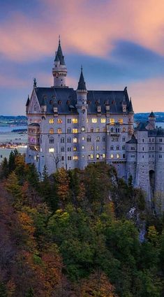 a castle lit up at night on top of a hill next to trees and water