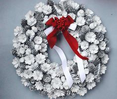 a white wreath with red ribbon and pine cones