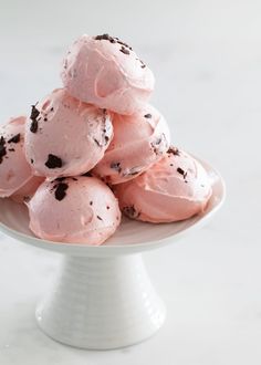 a white plate topped with pink ice cream covered in chocolate chipped cookies on top of a marble counter