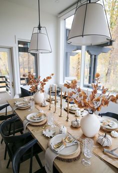 a dining room table set with plates and place settings in front of a large window