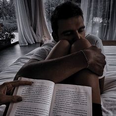 a man laying on top of a bed holding an open book next to his face