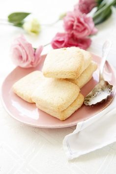 three cookies on a pink plate with a spoon and flowers in the backgroud