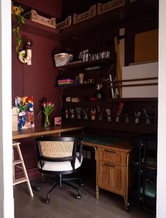 a desk and chair in a room with shelves on the wall behind it, along with other items