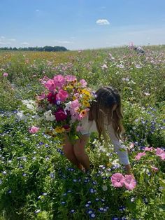 a woman kneeling down in a field full of wildflowers and holding a bouquet of flowers