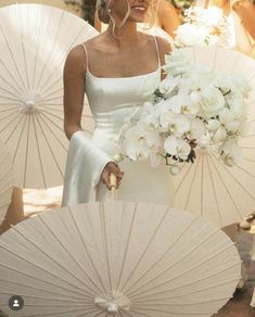 a woman in a white dress holding an umbrella with flowers on it and some people behind her