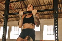 a woman with tattoos on her arms and legs hanging from a bar in a crossfit gym