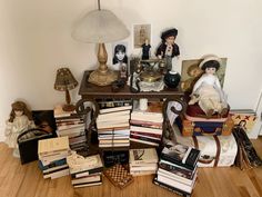 a pile of books sitting on top of a wooden floor next to a lamp and table