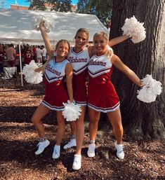 three cheerleaders pose for a photo in front of a tree