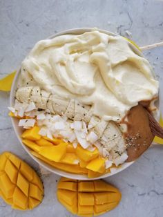 a bowl filled with whipped cream and sliced mangoes next to two pieces of fruit