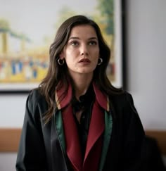 a woman in a black jacket and red scarf looking off into the distance with her hand on her hip