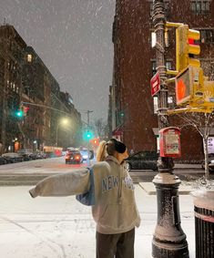 a woman standing on the side of a street next to a traffic light in the snow