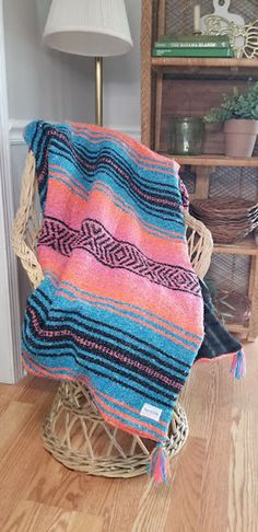 a colorful blanket sitting on top of a wicker basket in front of a lamp