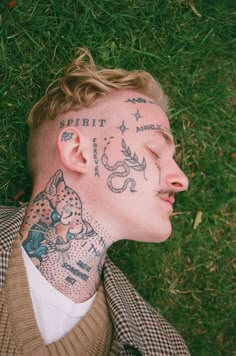 a man with tattoos on his face laying in the grass