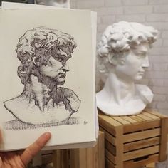 a person holding up a drawing in front of some busts