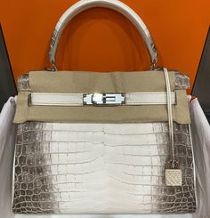 a white and beige handbag sitting on top of a table next to an orange wall