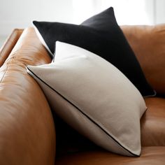 two black and white pillows sitting on the back of a brown leather couch in front of a window