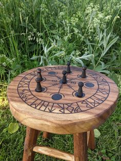 a wooden table with chess pieces on it in front of some grass and flowers,